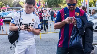 Dos aficionados del Real Madrid y del Fútbol Club Barcelona miran sus smartphones.