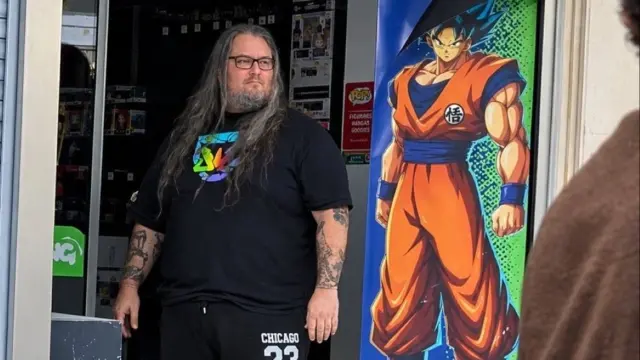 Pierre, junto a la imagen de Goku en la puerta de su tienda vandalizada